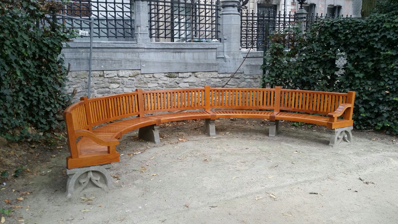 Een nieuwe halfronde houten bank geplaatst voor een van de antieke muren met hekwerk in de Kleine Zavelsquare. De nieuwe bank heeft een klassieke stijl, identiek aan de oorspronkelijke banken in het park.