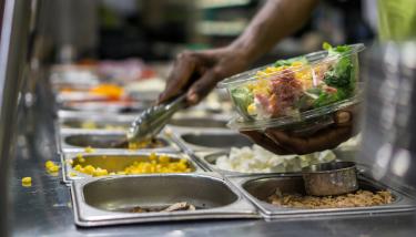 Cantine d'une entreprise, une main d'homme remplit un bol de crudités
