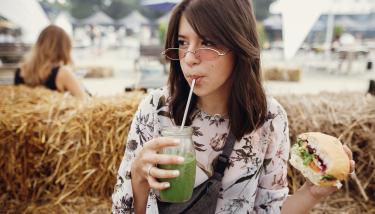 Jeune fille à un festival qui boit dans un contenant réutilisable et mange un hamburger